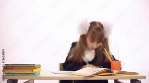 A girl dressed in a school uniform sitting at school desk, she writes in a notebook, textbooks on the table