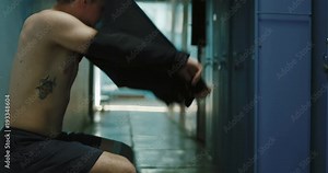 Side view of sportsman taking off shirt in locker room in semilit sports center. Stock Video