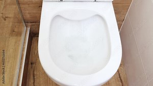 Closeup view of a flushing white toilet. The water swirls in the toilet bowl.