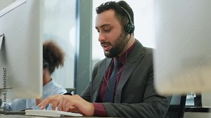 Senior confident friendly operator man agent with headsets and computer working in a call center modern office. Solving problem to customer with smile. Customer support and teamwork concept