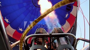 Burner fires into red, white and blue flag hot air balloon filling it with heat so it will rise and carry passengers in basket to destination.