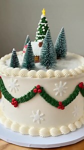 “Christmas Village Cake🎂🏠🎄❄️.” It’s a holiday-themed centerpiece featuring a snowy landscape with a decorated Christmas tree, gingerbread-style house, snowman, candle, and fondant garlands—perfect for Christmas parties or seasonal displays. #cake #cakedecorating #baking #holidayseason #gifts #christmasseason | Rechartcake
