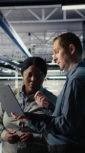 Vertical Team of engineers in server hub optimizing deep learning AI systems handling tasks. Teamworking data center colleagues adjust artificial intelligence model parameters using device, camera A