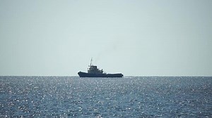 Tug boat in open calm sea, heading back to port at sunset, helps large container ships maneuver. Aerial view, maritime industry, oceanic transportation or business concepts.