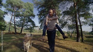 Man carrying woman on his back through the trees while walking his dog