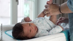 Newborn baby being changed on a table, held gently by mother's hands, showcasing the nurturing care and intimate bond between mother and infant during a daily routine at home
