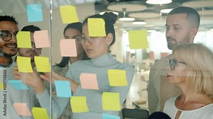 Business people working with sticky notes in office using glass board talking sticking multi-colored paper sharing ideas. Coworking and creative work concept.