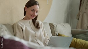 Woman uses a computer laptop on the couch at home. Young woman managing and doing a business