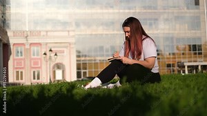 young woman makes notes in a notepad while relaxing in the park on a picnic