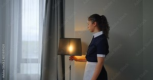 Beautiful Young Maid In Uniform And White Apron Switching Off Floor Lamp In Hotel Room