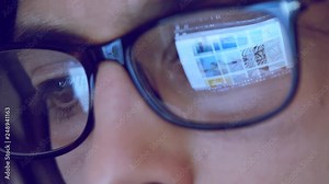 Close up footage of female with glasses looking at computer. Reflection of computer screen on woman glasses.