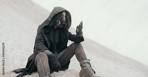 Post apocalyptic female wanderer wearing grunge hooded mantle gas mask hand pouring sand sitting in desert. Steampunk cyberpunk woman soldier. Dead world concept, future survivor after nuclear war