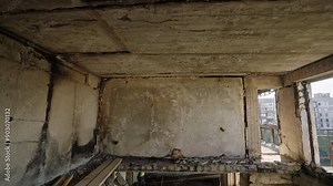 War-damaged apartment shows collapsed ceilings, burnt walls. Interior in ruins, visible damage from conflict. Urban decay, destruction in residential area. Roof, floor fallen, exposed to light.