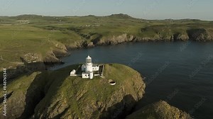 An aerial view of the of Strumble Head lighthouse in Pembrokeshire, South Wales, on a sunny summer evening. Circling left to right whilst flying away from the lighthouse.