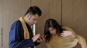 Indian couple in their ethnic wear using a smart phone mobile internet device over wifi at home, the woman adjusts her dress