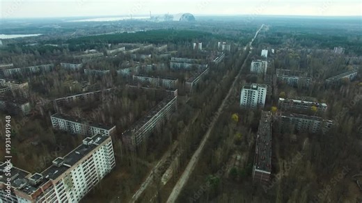 Drone footage of Pripyat, Ukraine, an abandoned city near Chernobyl Nuclear Power Plant. Residential blocks and roads are overgrown by dense forests. Distant Chernobyl New Safe Confinement structure v