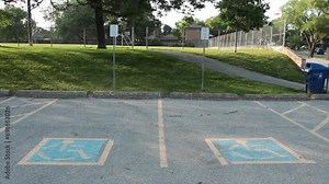 two handicap parking spots with blue and yellow handicap logo inside them, small grass hill path and soccer field behind them