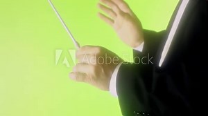 The hands of an orchestra conductor moving to direct the musicians, over a green background with a strong glow. Closeup detail shot.