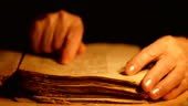 Elderly woman reading old book by candlelight