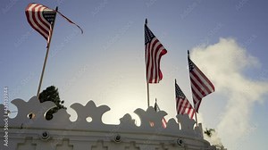 This video shows American flags flying in the wind in slow motion with a blue sky in the background as steam billows from the top of the old ship.