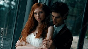 Fairy-tale wedding couple posing in a stylish house with panoramic windows and mountain views. Red-haired bride posing with the groom. Wedding concept