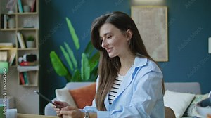 Beautiful young woman using modern digital tablet for work, looking and posing at camera. Business woman chatting with friends, family via modern device during sitting on chair at home.