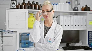Confident young blonde scientist, happily enjoying her groundbreaking research in her lab, sharing a joyful smile as she professionally takes off her security glasses.