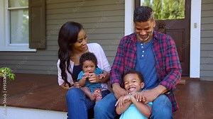 Family With Baby and Son Sit On Steps Of Porch In Front Of Home