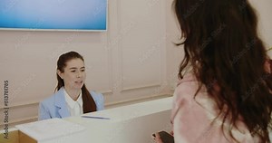 A friendly female receptionist at a healthcare clinic assists a female client. The reception area is clean and professional. Friendly Receptionist Assisting Client at Modern Health Clinic