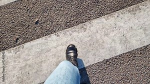Women's legs walk down the street, first person view. A pedestrian's legs walk across a road zebra crossing. Close-up of human legs, walking outdoors. Spring, autumn or winter, comfortable shoes