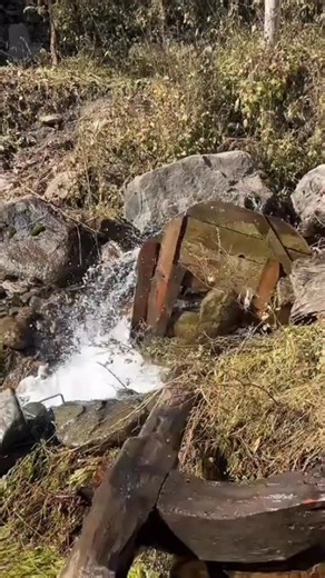 madeinnepal on Instagram: "A traditional water-run okhal system (pani ghatta) commonly found in rural hilly regions of Nepal. It works by using the natural flow of water to create mechanical energy for grinding grains. In this setup, a wooden water wheel is placed in a small stream or canal. Flowing water strikes the paddles or blades of the wheel, causing it to rotate continuously. This rotation is then transmitted through a wooden shaft connected to grinding stones or a pounding mechanism (oft