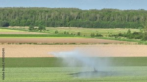 Irrigation pivot gun machine spraying water on an agricultural field during a dry sprintime day.