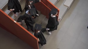 Free stock video - Top view of a group of preschool students in cap and gown running down the stairs holding their graduation diplomas while one of them hugging the teacher