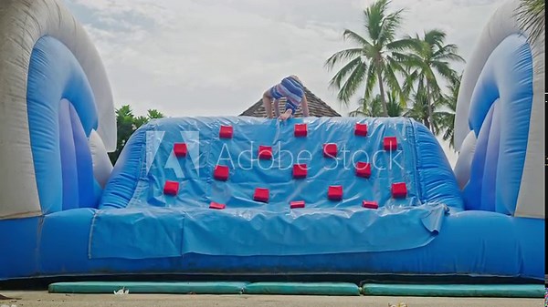 Boy in Swim Trunks Climbing Inflatable Water Slide at Poolside