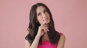 A smiling young woman is thinking about something standing isolated over pink background