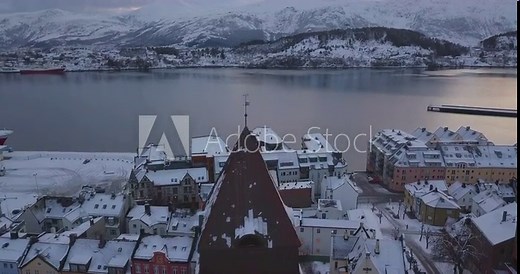 Cinematic aerial drone footage of downtown Alesund, Norway's most beautiful town in winter when everything is covered in snow. We are flying over the church and other remarkable art nouveau buildings.