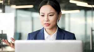 Confused asian businesswoman having difficulty using laptop sitting at workplace in business office. Worried puzzled woman worker has problem complexity with work on application on computer. Close up
