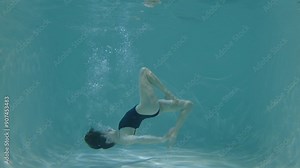 Skillful fit attractive female synchronized swimmer improving artistic swimming elements , stretching in upside down side split position underwater while training in swimming pool.