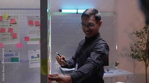 Businessman is organizing notes on a transparent glass wall in an office. He is using colorful sticky notes and a marker