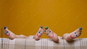 Paint fun feet kids with smiley drawing toes. Barefoot child playing and dancing toes colorful funny legs kids. Painted happy smiles children feet in bed waving funny foot concept on yellow background Stock Video