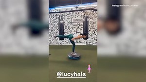Lucy Hale balances on a rubber ball in the gym with her trainer
