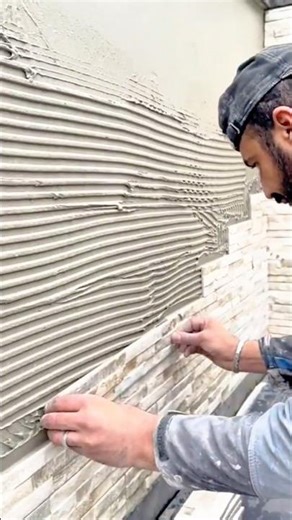 Skilled craftsman expertly setting natural stone cladding onto ridged adhesive mortar