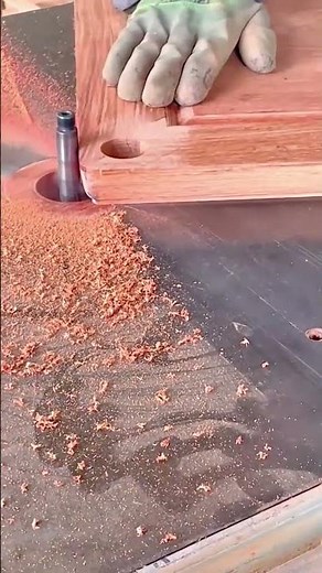 A gloved hand guides a wooden board over a spinning router