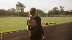 A beautiful female athlete is working out at the stadium. The girl is wearing black tight shorts and a long-sleeve black top. She finishes her run and stops to catch her breath.