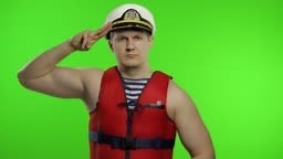 Young muscular sailor man works as lifeguard at beach salutes with...