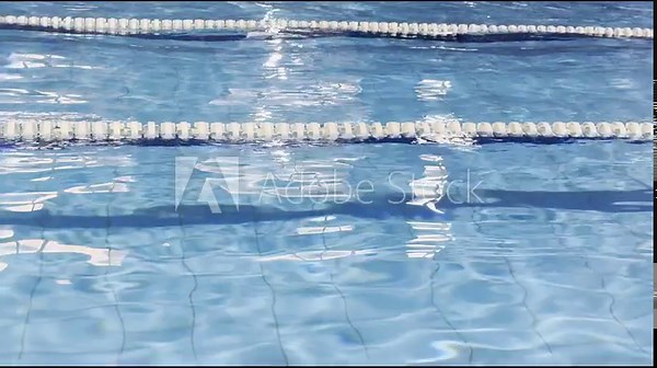 Swimming pool segmented by lane ropes, rippling water reflecting sunlight, embodying themes of sport, fitness, competitive swimming, aquatic exercise and staying active for healthy lifestyle