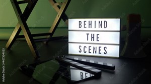 Behind the scenes letterboard text on Lightbox or Cinema Light box. Movie clapperboard megaphone and director chair beside. Background LED color change loop. static camera in video production studio.