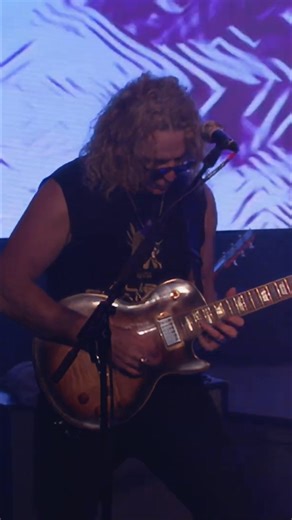 A rock band delivers a high-energy performance on stage. The singer belts out the lyrics, the guitarist shreds, and the bassist lays down the groove. Abstract visuals dance on the screen, enhancing the experience. #RockBand #LiveMusic #MusicPerformance #Guitar #Bass | Lui Krieg Music