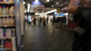 A bustling market scene in the evening shows people exploring various vendor stalls, with bright lights illuminating the area and a vibrant atmosphere.