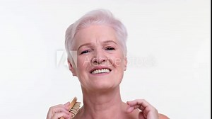 Senior woman tenderly runs a comb through hair, ace reflecting a sense of calm and care. Her focused gaze and gentle gestures capture a moment of self-pampering and self love.